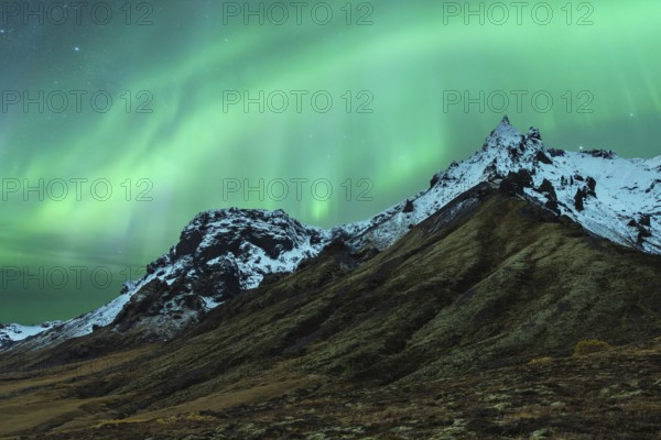 A mesmerizing northern light display dances above snow-capped mountains under a starry Icelandic