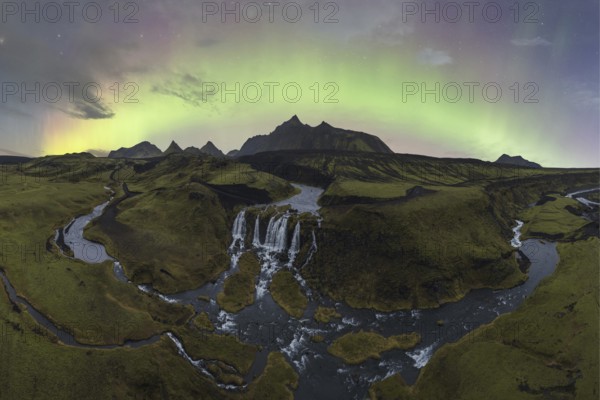 The aurora borealis illuminates the sky above a stunning Icelandic waterfall and meandering river
