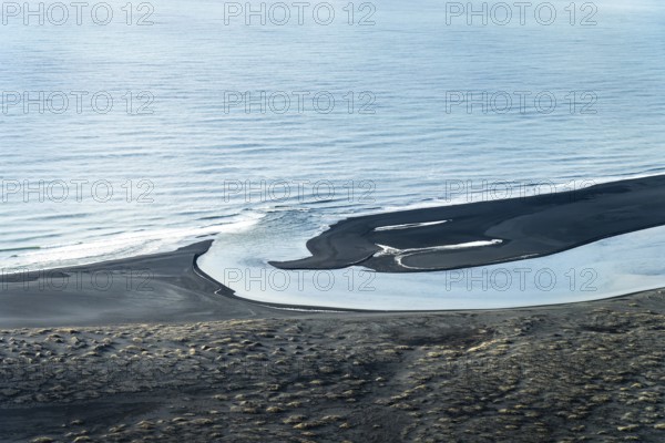Aerial view of a winding Icelandic river meeting the sea. Black sand contrasts with the blue water,