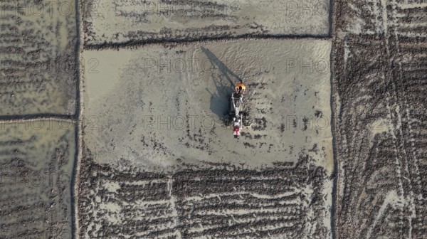 In an aerial view, a farmer ploughs a rice paddy field with a power tiller on February 16, 2026 in