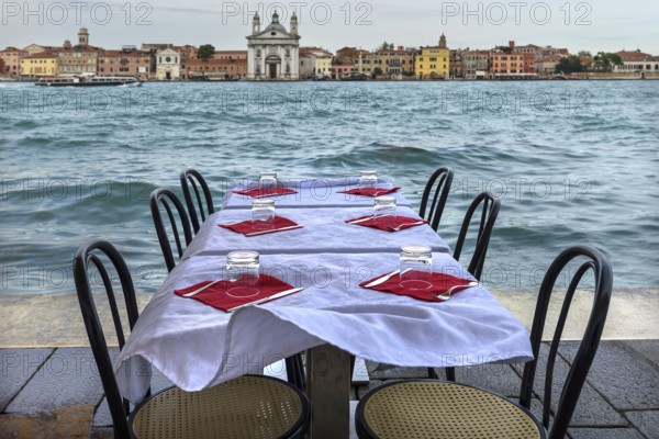 Restaurant tables on the shore in windy weather, on the island of Giudecca, Venice behind, Veneto,