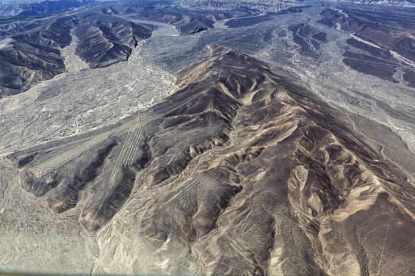 Barren desert landscape from above, distinct lines and geoglyphs visible in the mountains, the