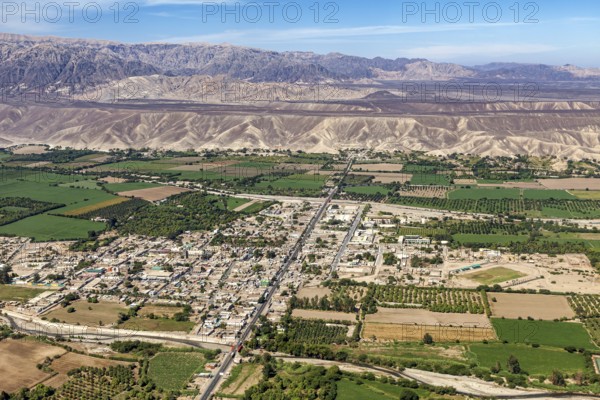 Expansive aerial view of a city with green fields and mountains in the background, The city of