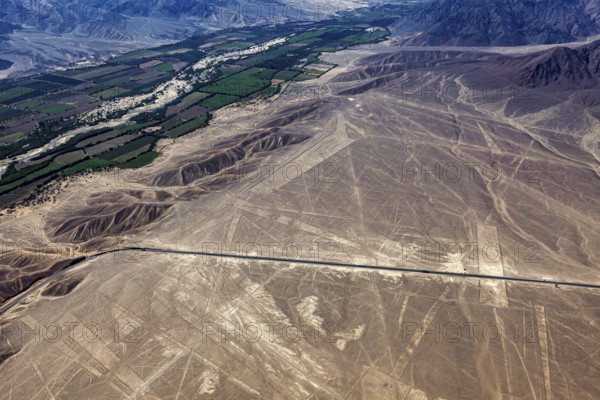 Aerial photo shows dry geoglyphic landscape next to green fields and a road, the geoglyphs and