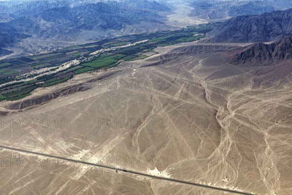 View of Nazca lines with contrasting green fields and mountain ranges in the background, the