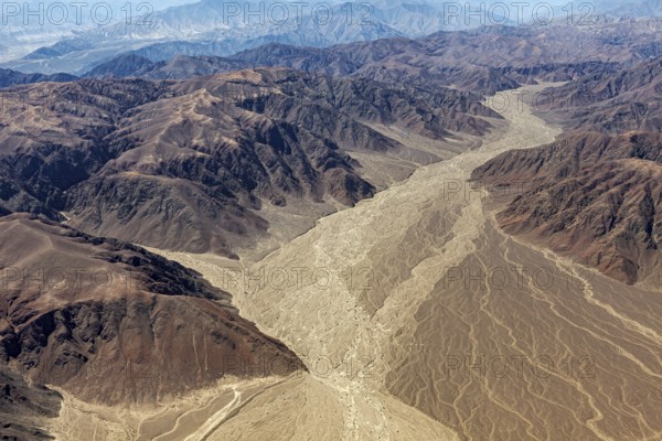 Aerial view of a dry mountain landscape with a dried-out riverbed surrounded by brown and