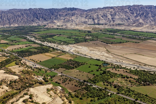 Green fields and river valley in front of a rocky mountain range under clear sky, the desert