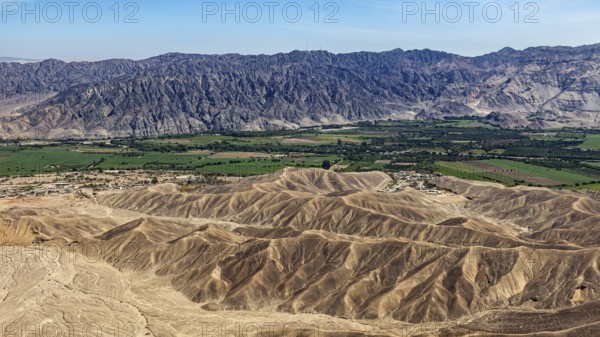 Contrasting landscape with desert in the foreground and green fields in front of a mountain chain,