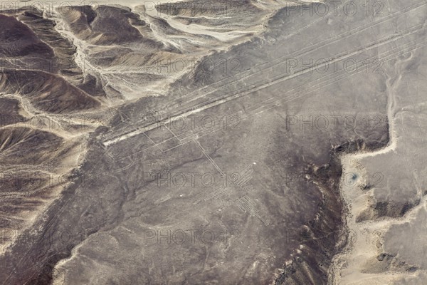 Geoglyph lines in an extensive, sand-colored desert landscape with nearby mountains, the geoglyphs