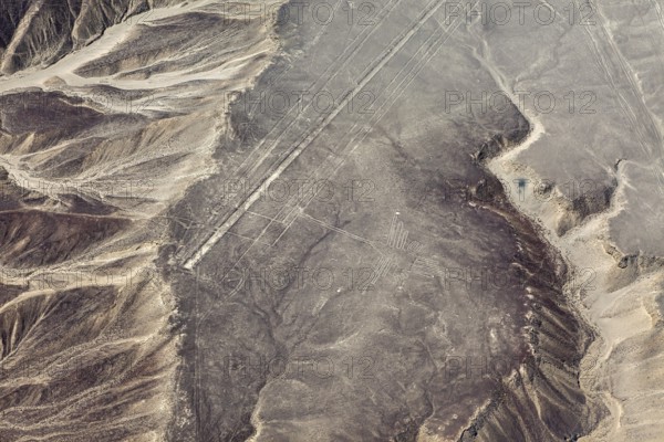 Desert area with linear geoglyph patterns, captured from the air, with mountains in the background,