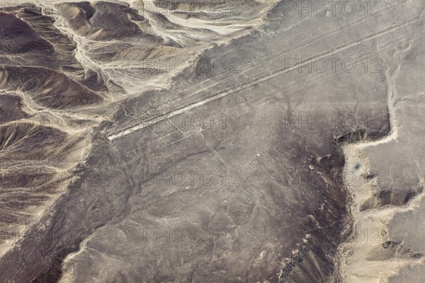 Lines and geoglyphs visible from the air in a desert-like environment surrounded by mountains, The
