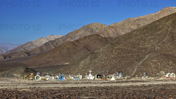 Cemetery in a desert-like landscape in front of a mountain range under clear skies, cemetery in the