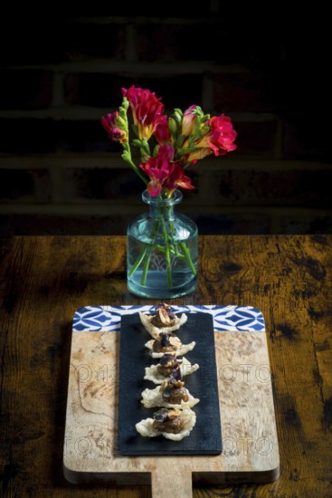 Elegant cracker canapes topped with vegetable satay stew and peanuts, served on a black slate over