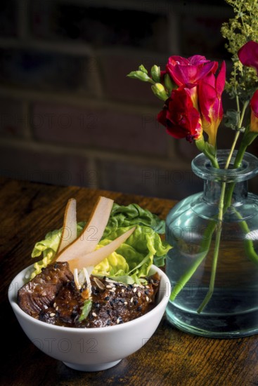 A beautifully presented Asian beef bowl garnished with fresh greens and pear slices, paired with a