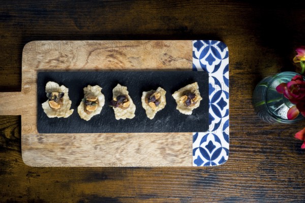 Crispy cracker canapes topped with vegetable satay stew and peanuts, arranged on a black slate over