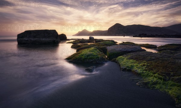 Sunrise casts golden hues over the rocky shoreline of Cala del Lastre in Portman, Murcia The