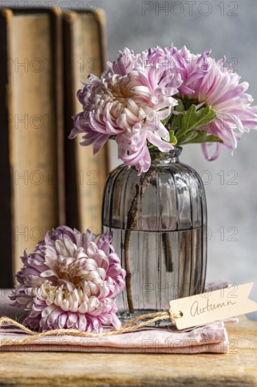 Soft pink chrysanthemums in a vintage glass vase beside rustic books and a tag reading Autumn