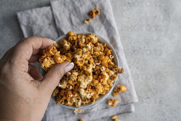 Cropped unrecognizable person's hand picking sweet caramel popcorn from a gray bowl, set against a