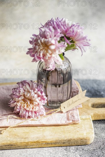 Elegant chrysanthemums in a textured glass vase, set on a wooden board, create an autumnal theme A