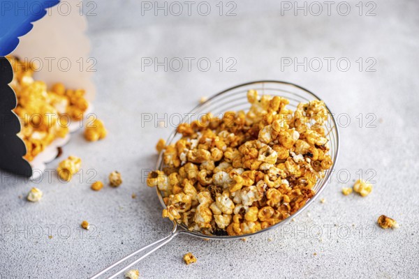 Top view of sweet caramel popcorn served in a transparent bowl on a textured gray background. The