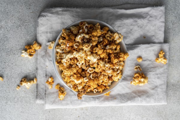 Top view of a bowl filled with sweet caramel popcorn, garnished with scattered pieces on grey
