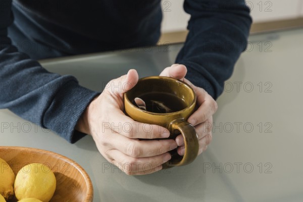 A close-up of hands holding a brown mug of tea with a spoon inside, placed on a glass table A