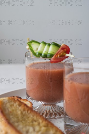 Clear glasses of gazpacho garnished with cucumber and tomato skewers A slice of crispy toast is