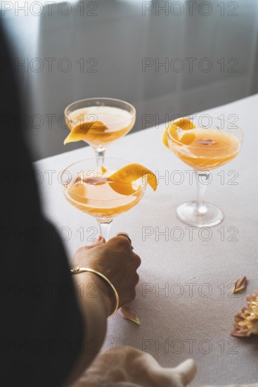 Cropped unrecognizable person holding a glass of vibrant mandarin cocktail, garnished with an