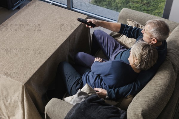 A senior couple sits closely on a comfortable couch, sharing a peaceful moment watching TV