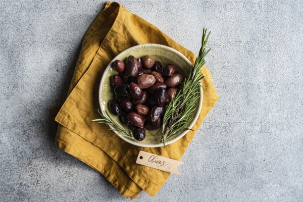 Top view of a ceramic bowl filled with Greek BBQ olives, accented with fresh rosemary sprigs,