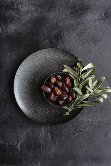 Top view of a dark textured plate filled with glossy Greek BBQ olives garnished with fresh green