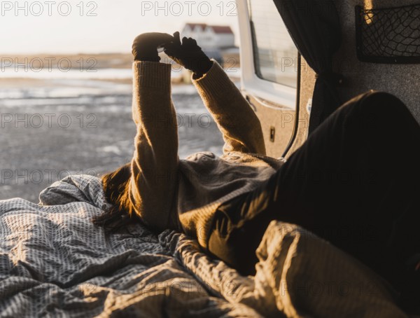 Unrecognizable woman lounging in a van during a camping trip in Iceland. She stretches her arms