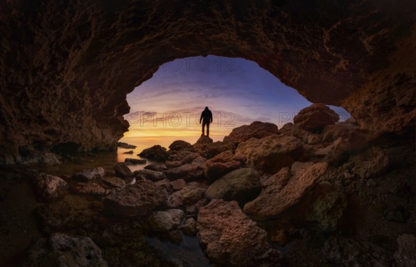 A stunning silhouette of a person standing on rocky terrain under a vibrant sunset sky, viewed from