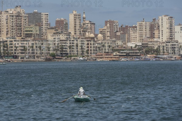 A lone Egyptian fishermen in a small boat fishing in the Mediterranean sea with the skyline of