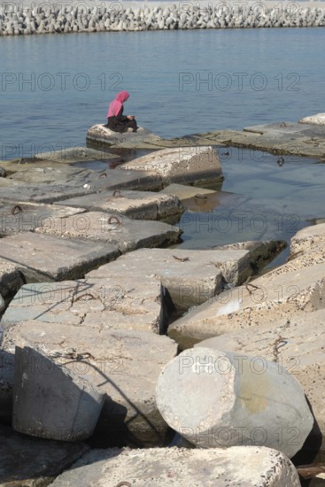 Alexandria, Egypt. December 1st 2022 Muslim women wearing a pink hijab sitting on large concrete