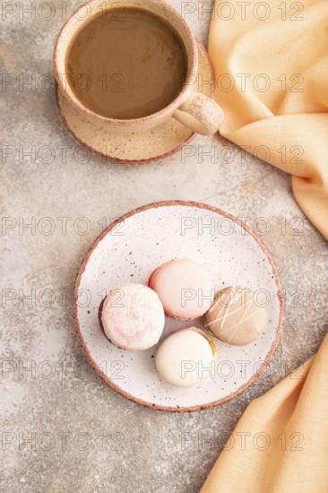 Macarons colourful cookies dessert, cup of coffee, on brown concrete background with orange linen