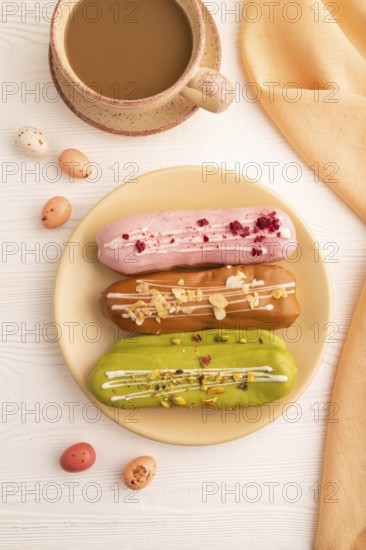 Glazed Eclairs on white wooden background and orange linen textile, cup of coffee, top view, flat