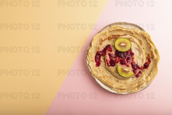 Stack of Plain Fried pancakes with jam and kiwi on pink and orange pastel paper background. top