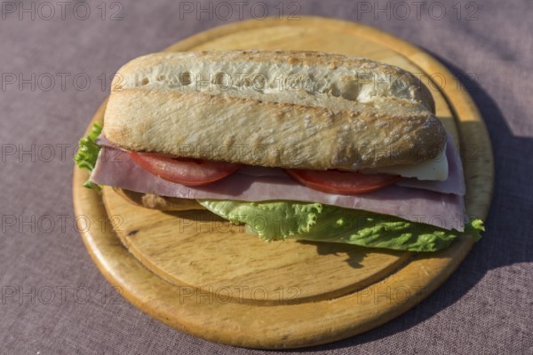 Ham and cheese baguette on a wooden plate, Italy