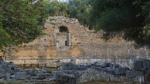 Palestra, red brick wall with an arch surrounded by vegetation and ruined architecture,