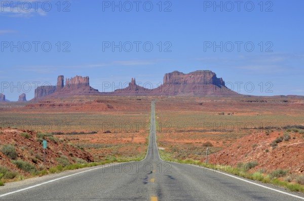 The long, straight road runs through a desert-like landscape with rocks. Access to Monument Valley,