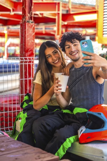 Young couple wearing racing suits taking a selfie during a karting break, showing happiness and