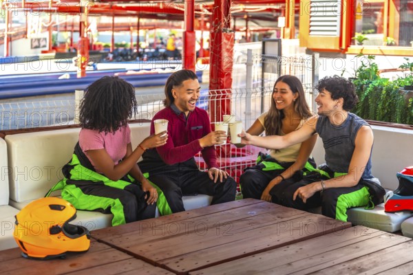 Four diverse young friends in racing suits making a celebratory toast with drinks at a wooden table