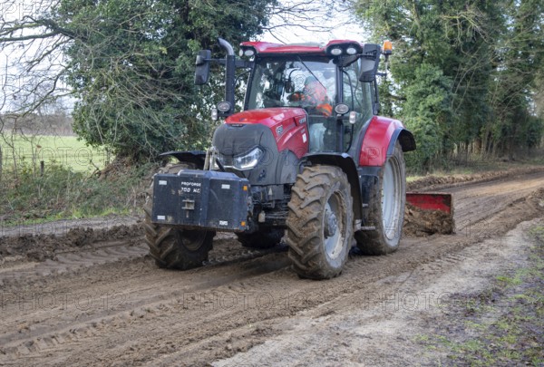 Tractor grading and levelling work repair a muddy, flood-prone country lane, Sutton, Suffolk