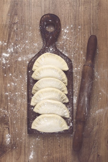 Raw chebureks, mini, on a cutting board, wooden table, close-up, no people
