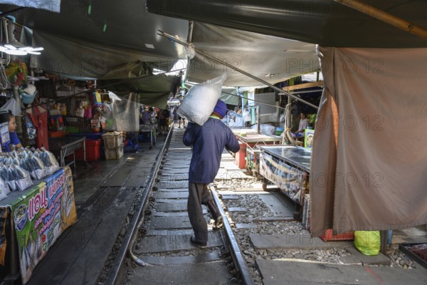 Mae Klong, Thailand. March 15th 2025. A market trader carries a bag of ice in the Maeklong Railway
