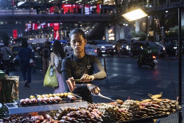 Bangkok, Thailand. March 26th 2025. A Thai woman cooks grilled meat at a street food stall at night