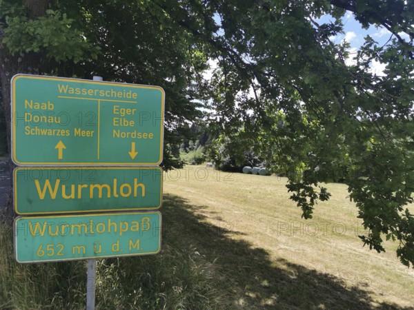 A green signpost, watershed, Wurmloh Pass, on a sunny meadow under a tree, Franconian mountain
