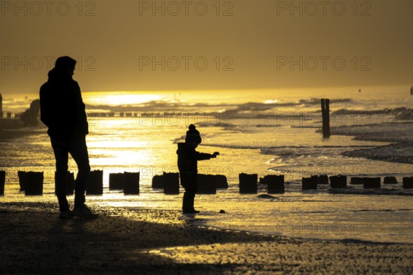 Winter on the North Sea, sunset at sea, beach walkers, coastal protection, through wooden posts,