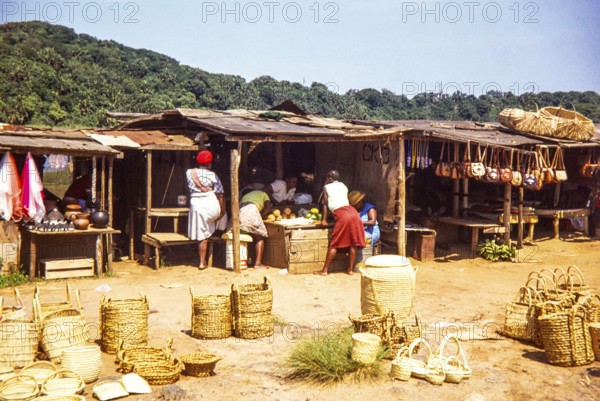 Woman at local market selling fruit and handicrafts including baskets, leather handbags and
